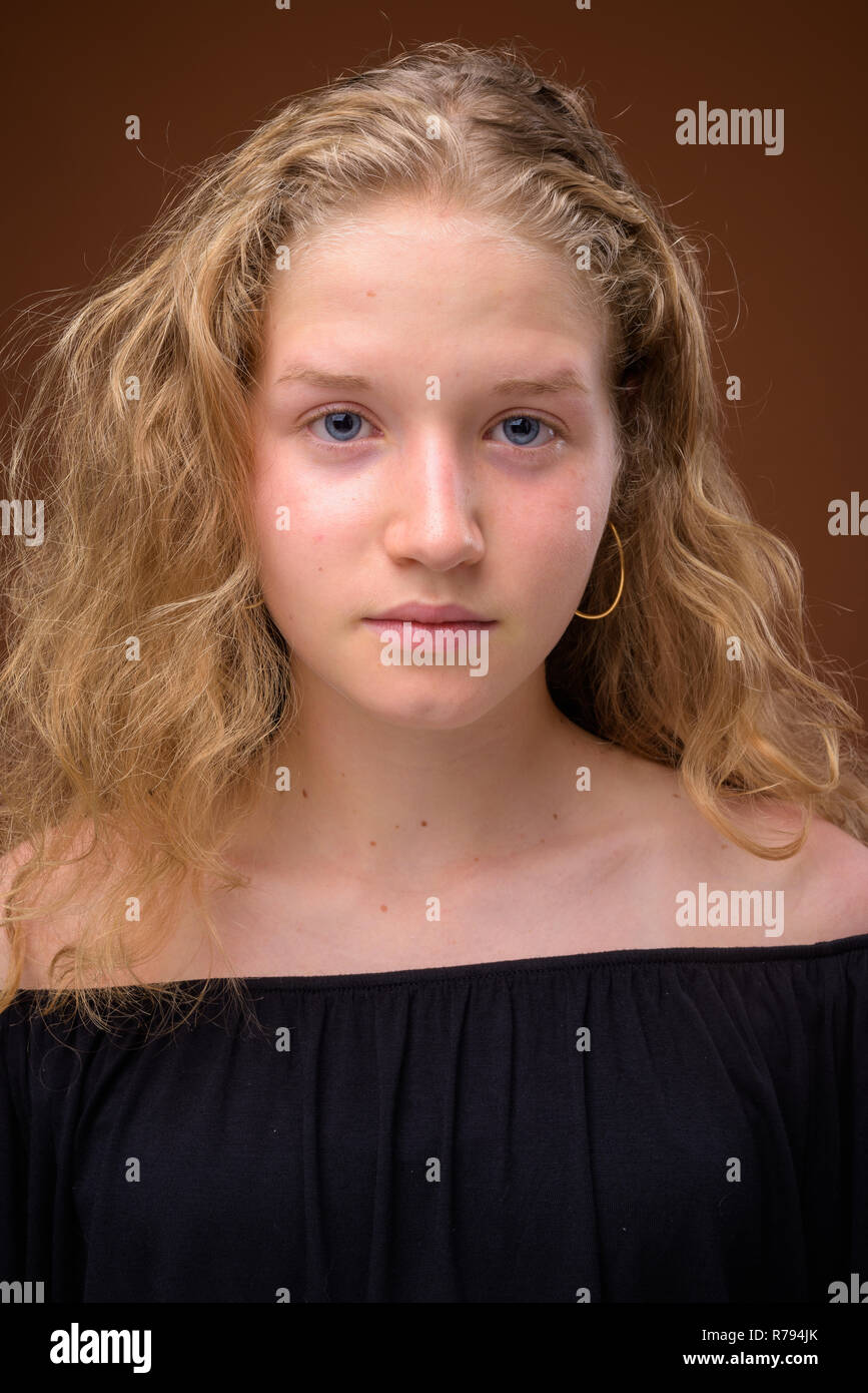 Gesicht der jungen schönen blonden Mädchen im Teenageralter gegen braunen Hintergrund Stockfoto