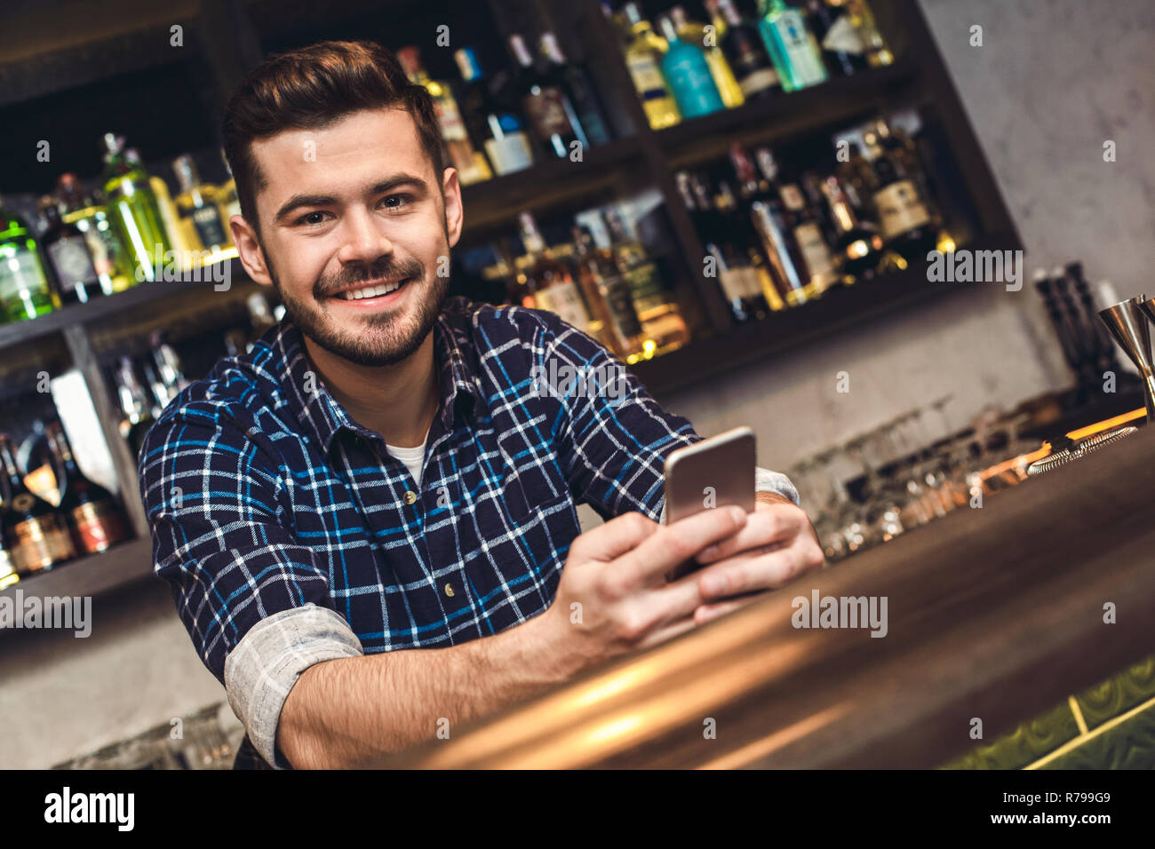 Junge Barkeeper saß an der Theke holding Smartphone glücklich Stockfoto