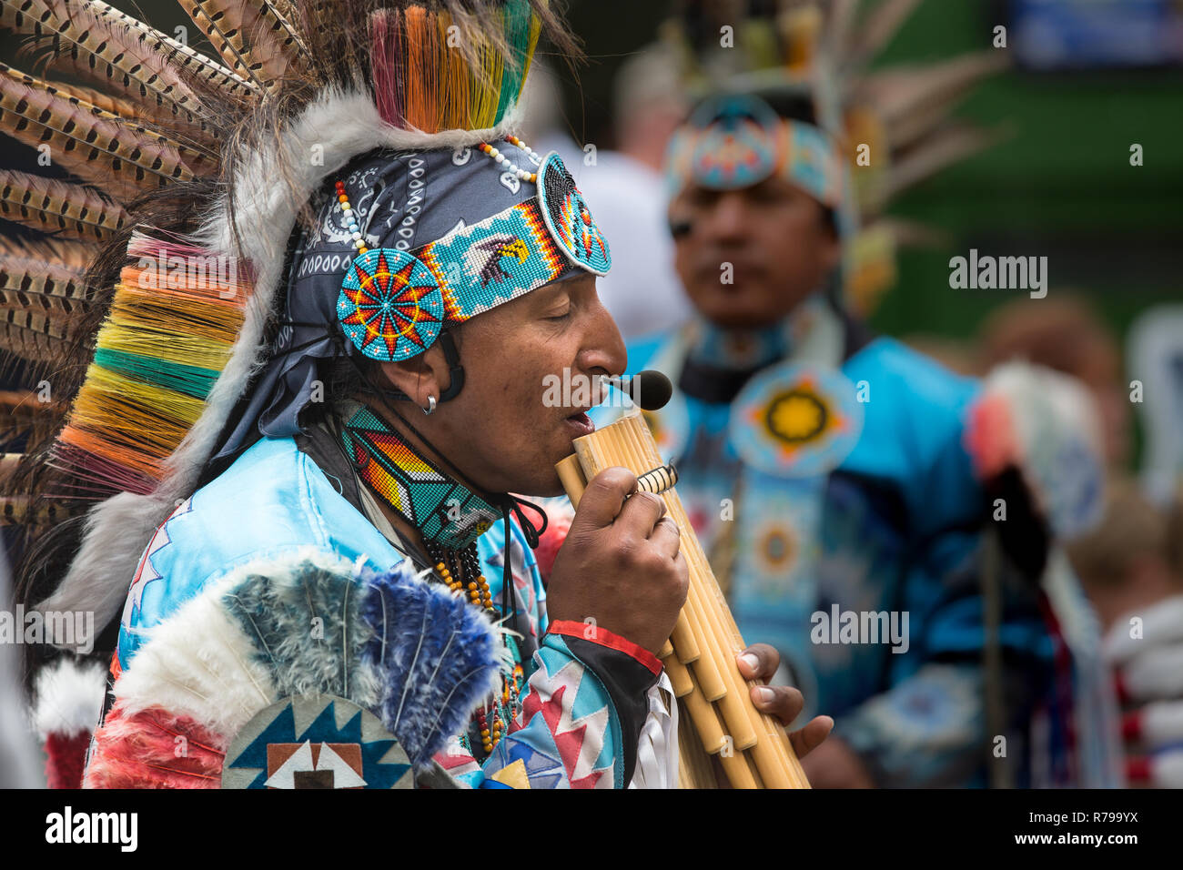 Ein Profil Portrait eines Südamerikanischen peruanischen Gaukler in farbenprächtigen, traditionellen Outfit gekleidet und Spielen auf der Panflöte für interessierte Zuschauer Stockfoto