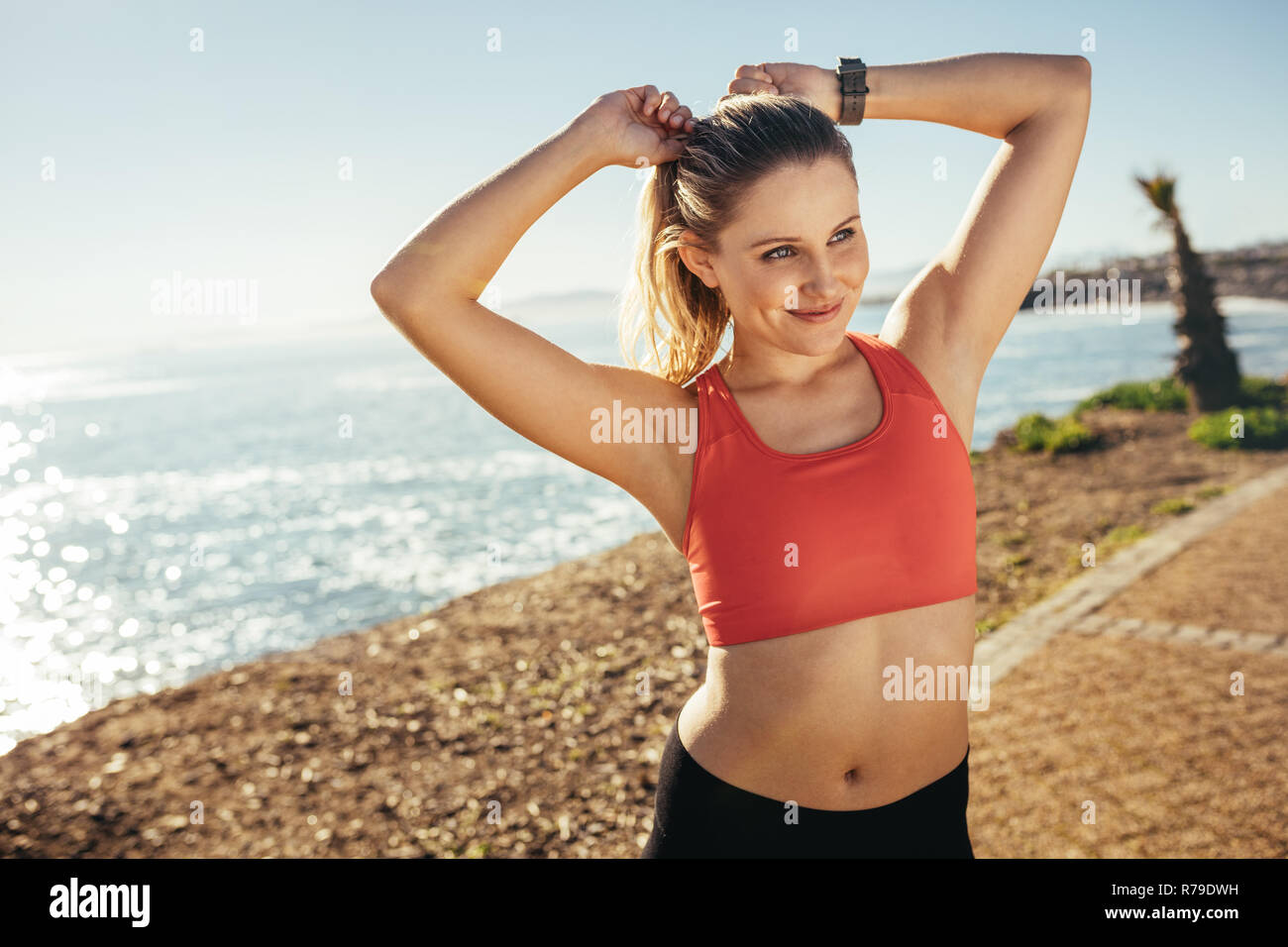 Lächelnde Frau Athlet steht in der Nähe des Meeres zu tun Fitness Übungen. Frau in fitness Verschleiß tun Workout an der Küste. Stockfoto