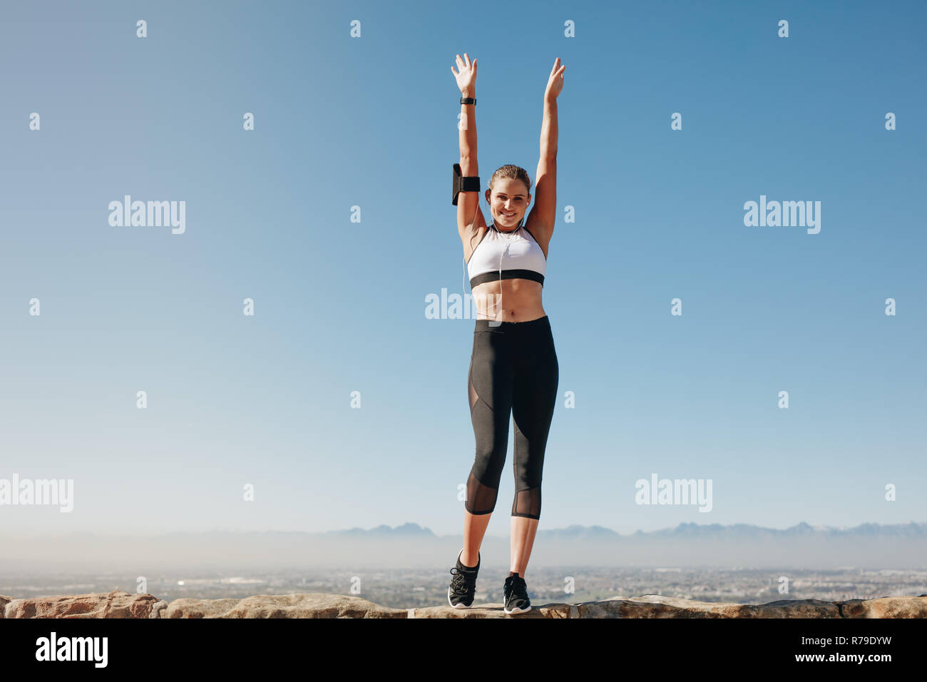 Weibliche Athleten auf einem Hügel und Workout, während Sie Musik hören. Lächelnde Frau in Fitness Kleidung Übungen auf einem Hügel mit ständigen Stockfoto