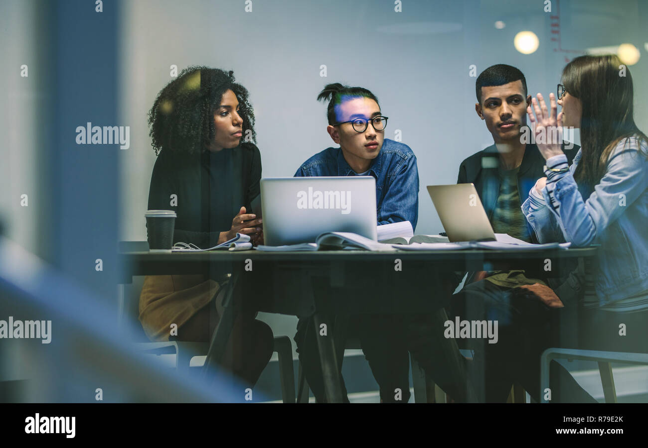 Frau im Gespräch mit Mitschülern beim zusammen studieren um den Tisch. Junge Leute am Tisch sitzen die Arbeit an einer Zuweisung. Stockfoto