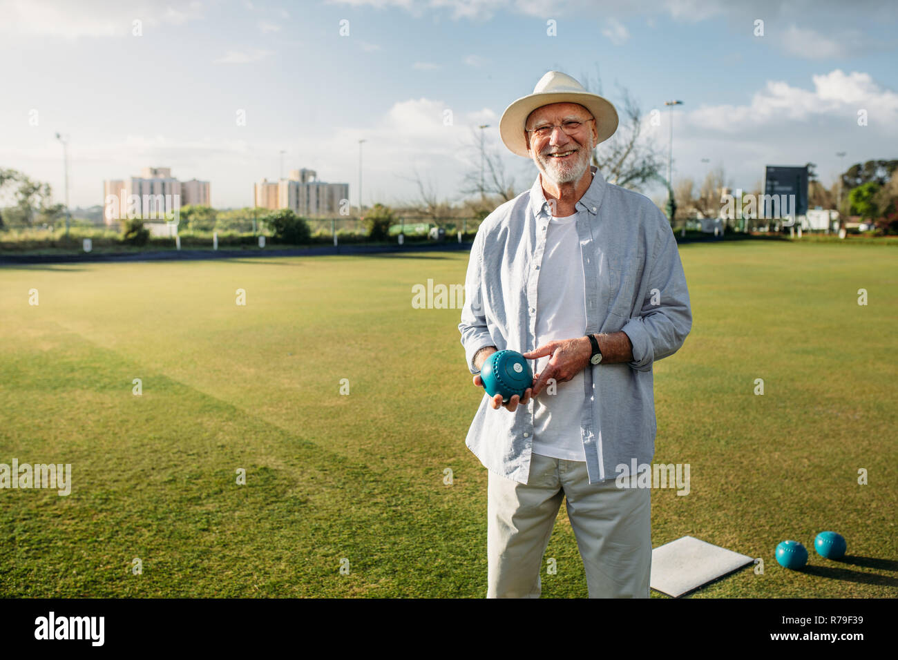 Lächelnd alten Mann in einem Park mit einem Boule in der Hand. Freundliche ältere Mann in hat sich in einen Spielplatz mit einem Boule. Stockfoto
