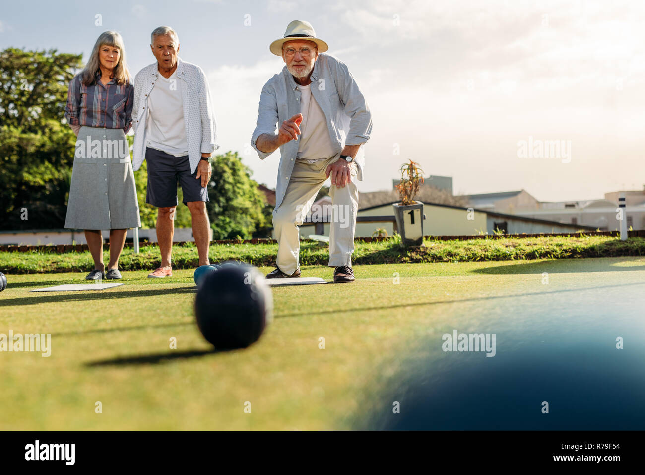 Ältere Menschen in den Hut werfen einer Boule, während seine Freunde auf. Zwei alte Männer und eine Frau ein Spiel spielen Boule in einem Rasen auf einem sonnigen Tag. Stockfoto