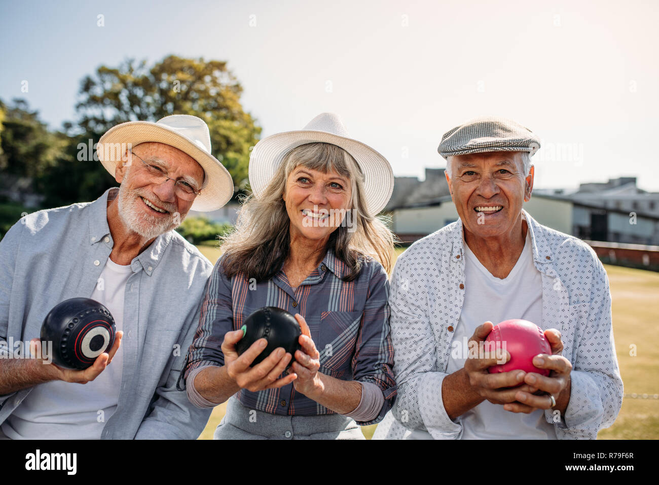 Lächelnde ältere Leute sitzen in einem Rasen, Boccia. Zwei Männer und eine Frau genießen das Spiel Boule sitzen zusammen in einem Park. Stockfoto