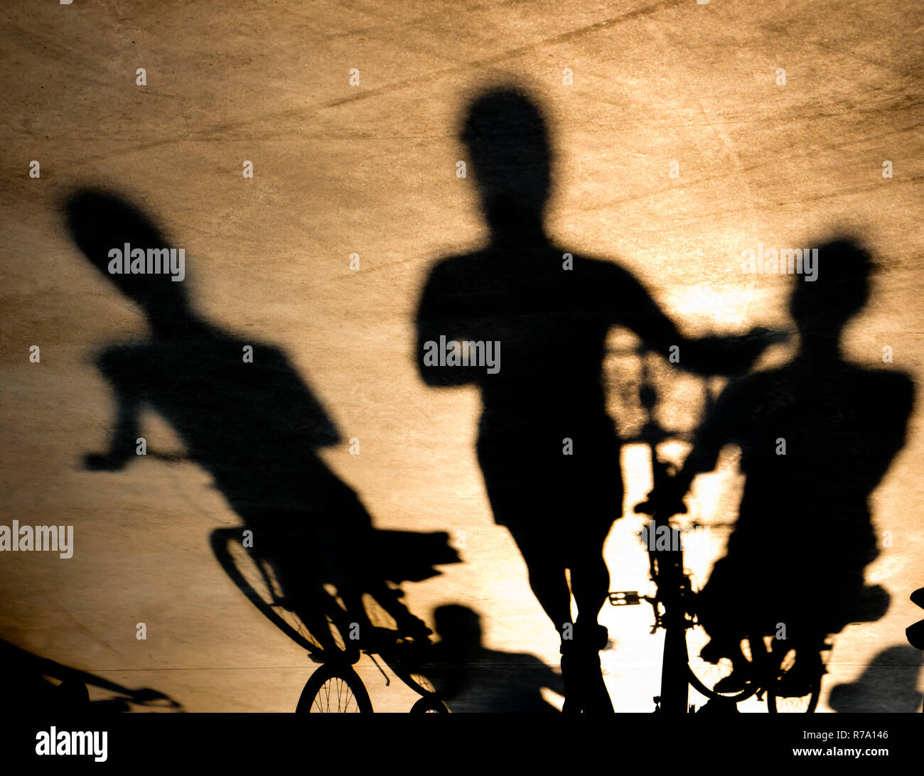 Verschwommene Schatten von drei jungen Frauen reiten oder schieben ihre Fahrräder im Sonnenuntergang Stockfoto