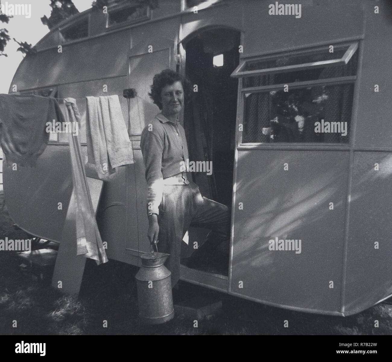 1940 s, Frau Metall milchkanne an der Tür zu ihrem Wohnwagen mit Kleidung hängend auf einer Wäscheleine, England, UK. Stockfoto