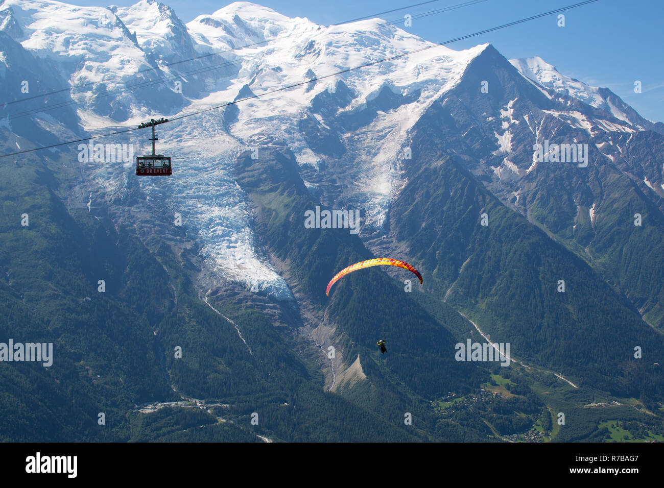 Ein Gleitschirm Piloten fliegen und die brevent Seilbahn vorbei vor der Mont Blanc und der Aiguille du Midi Gletscher, über Chamonix. Stockfoto