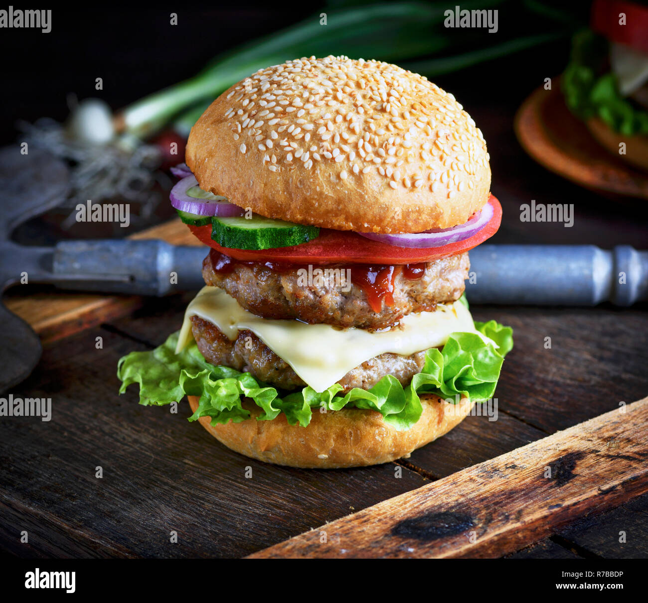 Cheeseburger in einem Brötchen Mit Sesam, in der Mitte von frischem Gemüse und Fleisch Schnitzel Stockfoto