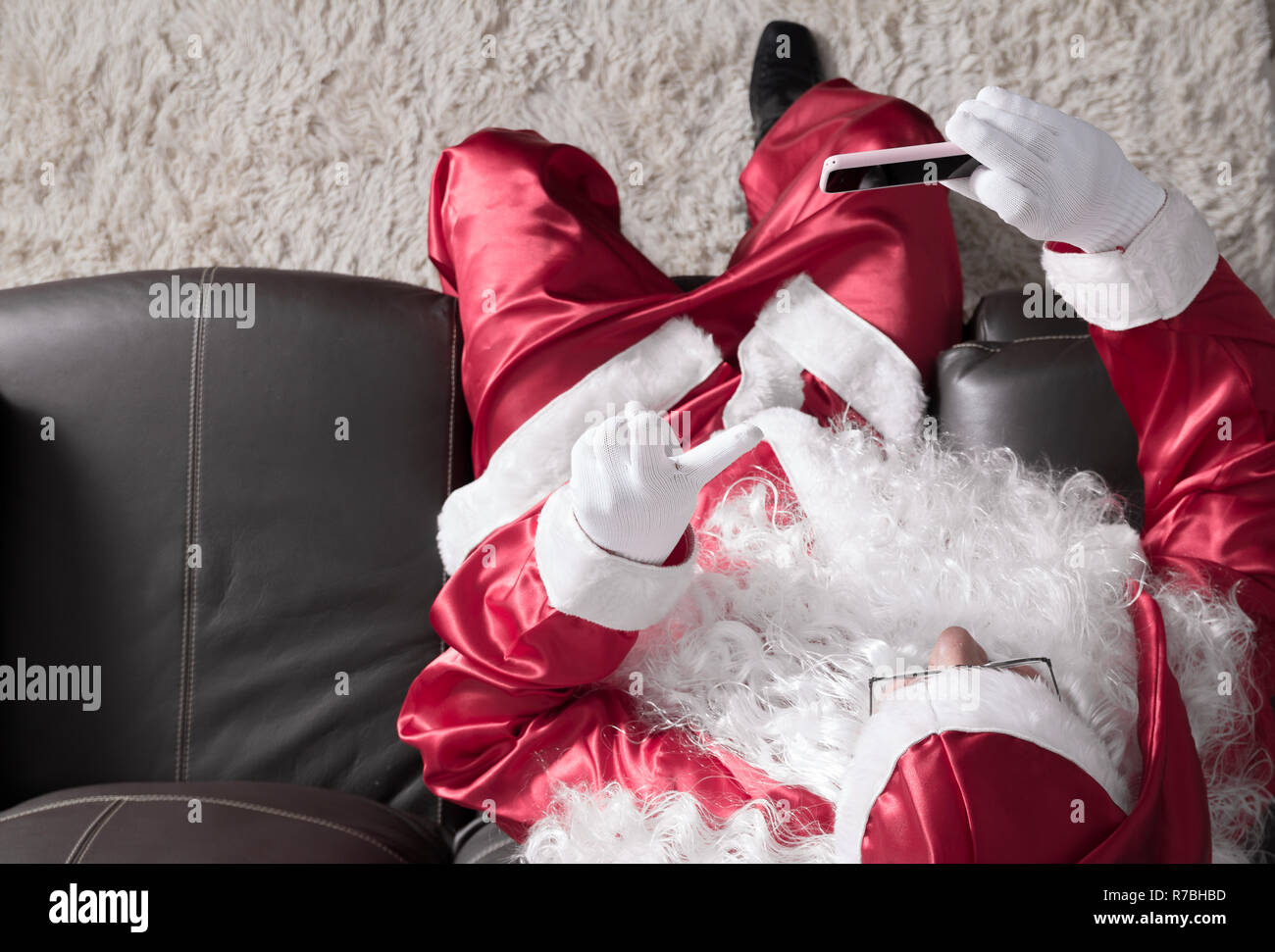 Overhead von Santa Claus (oder Kris Kringle) Entspannung im Sofa zu Hause mit Handy für Kommunikation und Freizeit. Ein videocall oder ein Selbst Stockfoto