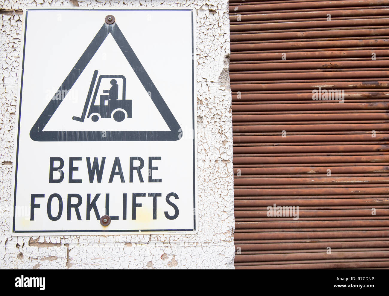 Ein warnen und verblasste Gabelstapler Warnschild an eine Wand mit abblätternder Farbe neben einem rostigen Rolltor Stockfoto