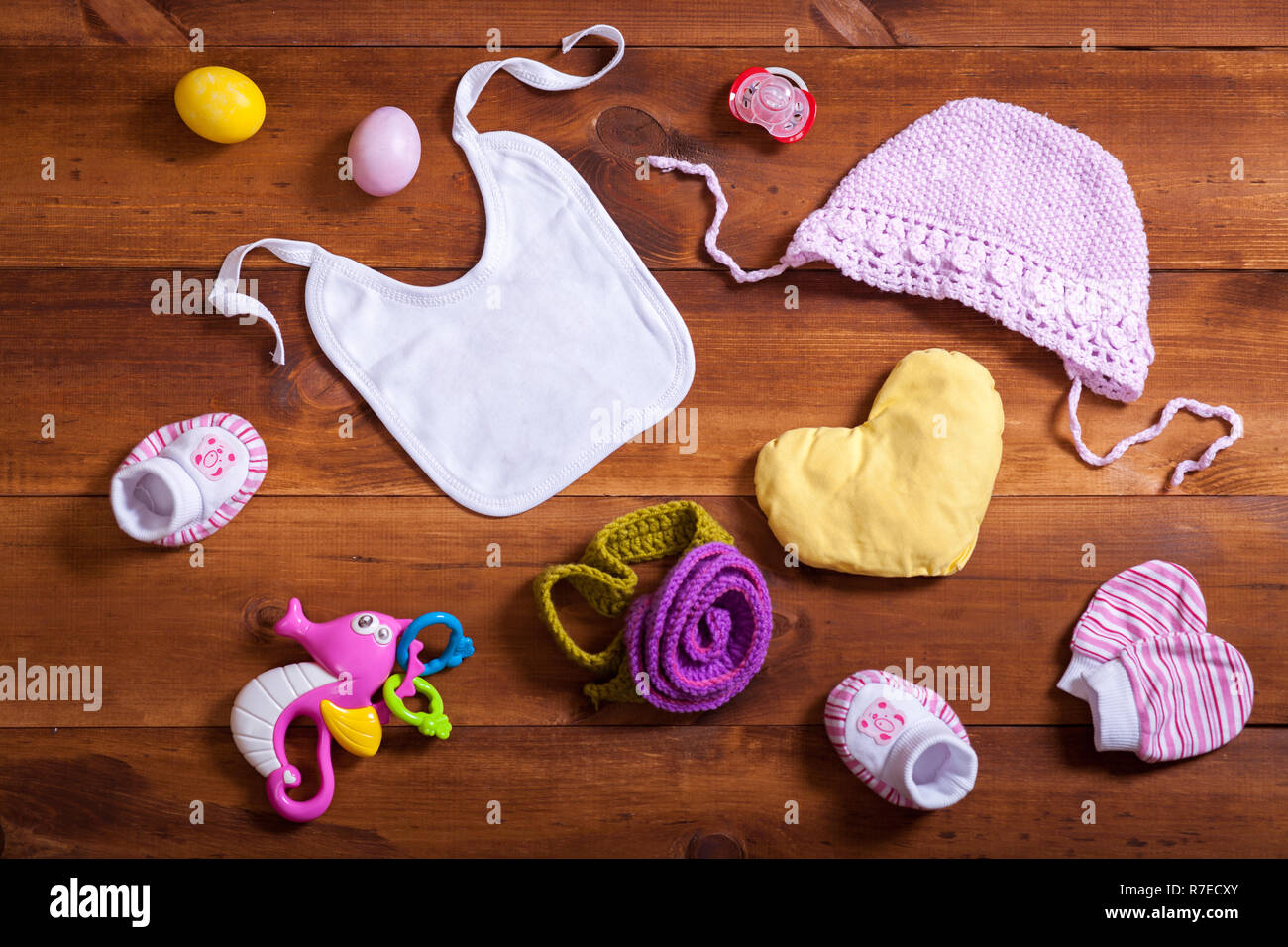 Baby Kleidung Zubehör Set, pink gestrickt Baumwolle Kleidung, Spielzeug und Kid bib auf braunem Holz- Hintergrund, Kind neugeborene Tuch für Mädchen, moderne Geschenk auf Stockfoto