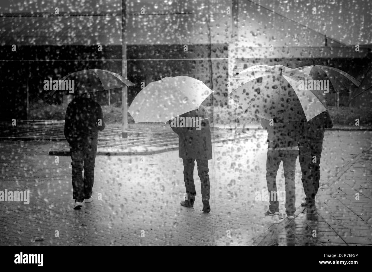 Vier Menschen unter bunten Regenschirm ist durch das Fenster voll von Regentropfen gesehen Stockfoto