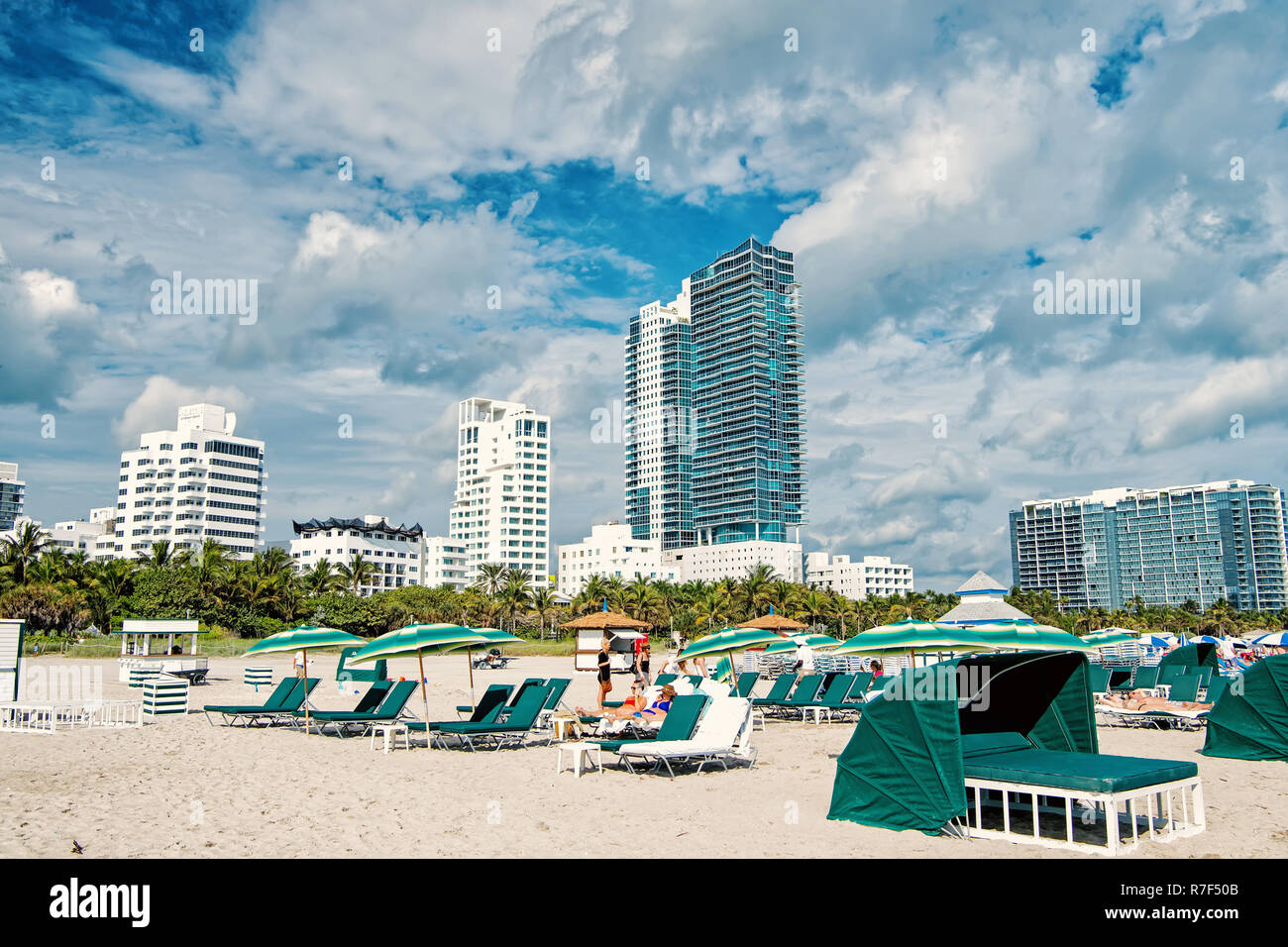 Miami, USA - Januar 10, 2016: Sandstrand mit Menschen entspannend auf Liegestühlen unter Sonnenschirmen Grün, Palmen, trübe Blau sonnigen Himmel. Sommer Urlaub. Lounge und Freizeitaktivitäten, Miami Beach und South Beach Stockfoto