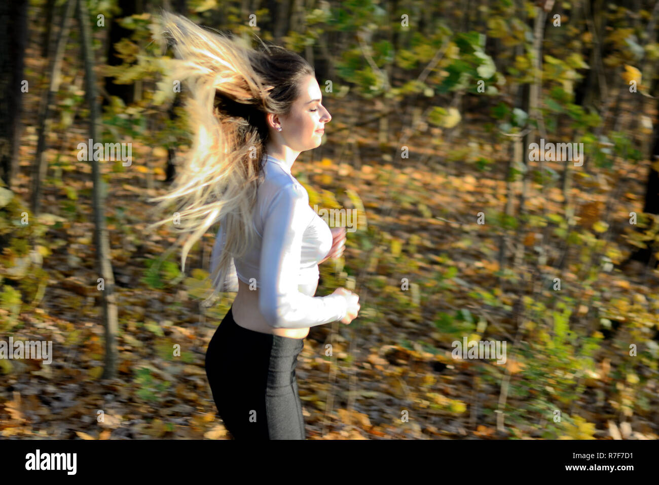 Junge Mädchen in den Wald zu laufen. Blonde Frau mit schwarzen Gamaschen und weiß Top. Aktiven Läufer mit veröffentlicht Haare. Stockfoto