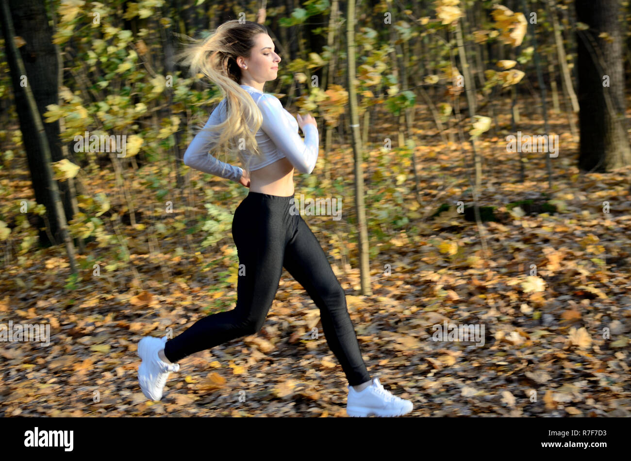 Junge Mädchen in den Wald zu laufen. Blonde Frau mit schwarzen Gamaschen und weiß Top. Aktiven Läufer mit veröffentlicht Haare. Stockfoto