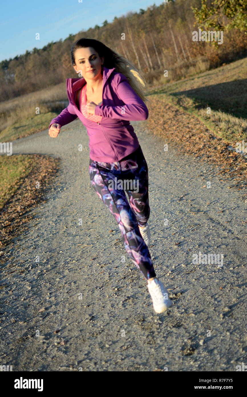 Junge Mädchen in den Wald zu laufen. Blonde Frau mit bunten Leggins und Lila top. Aktiven Läufer mit veröffentlicht Haare. Stockfoto