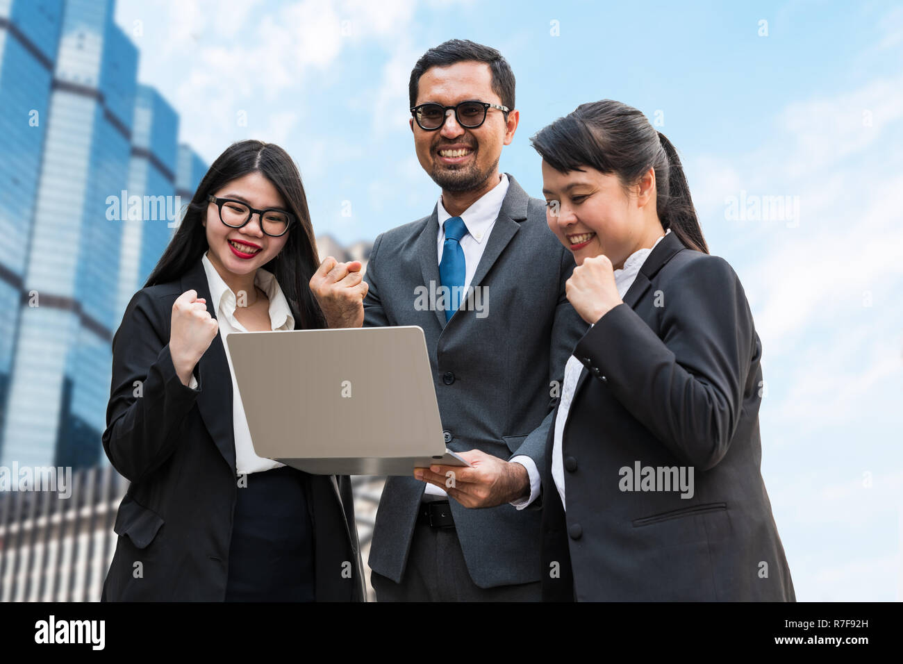 Zwei Frauen und ein Mann ballte die Fäuste auf dem Laptop Bildschirm schaut mit dem Glücklich lächelnde Gesichter Stockfoto