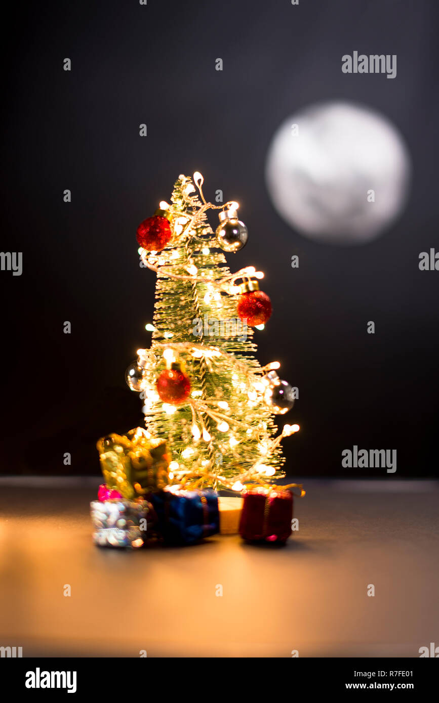 Pine Tree mit ausgefallenen Leuchten, Geschenke und Vollmond in der Nacht. Stockfoto