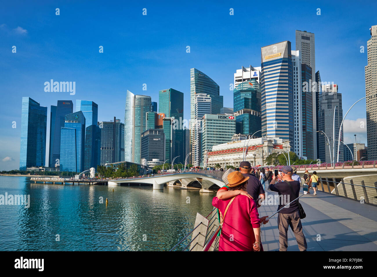 Asiatische Touristen fotografieren auf der Jubilee Bridge, Singapur, die Wolkenkratzer des Bankenviertels und Fullerton Hotel im Hintergrund Stockfoto