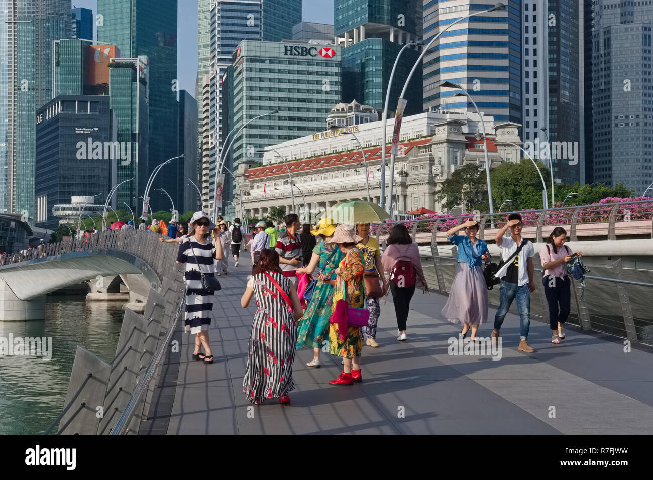 Asiatische Touristen fotografieren auf der Jubilee Bridge, Singapur, die Wolkenkratzer des Bankenviertels und Fullerton Hotel im Hintergrund Stockfoto