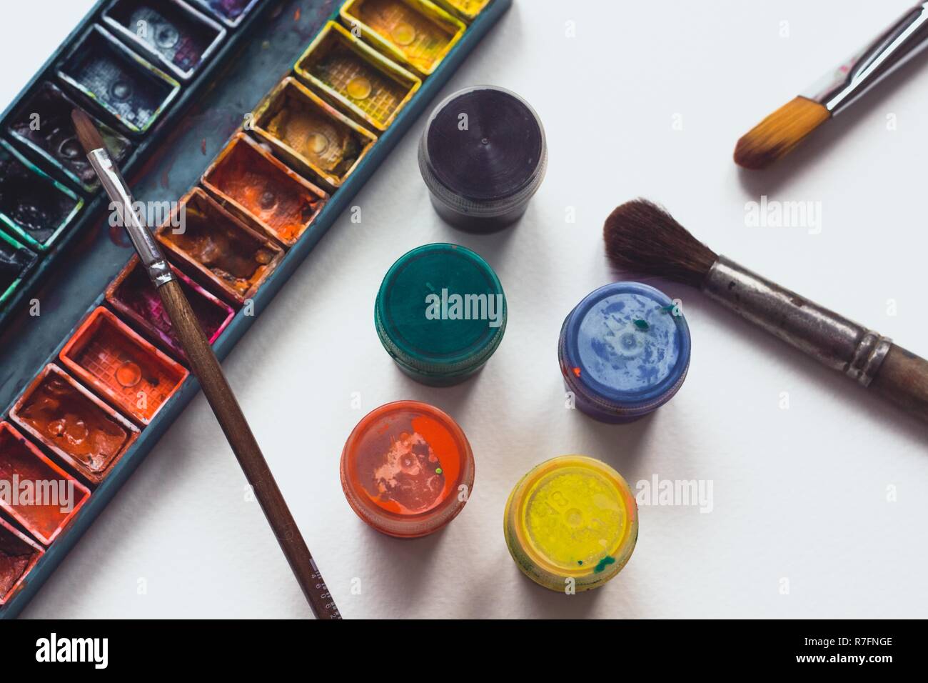 Helle und bunte Palette der Farben liegt auf weißen aquarell papier mit mehreren Bürsten für die Zeichnung. Unerlässliche Attribute für Kreativität. Stockfoto