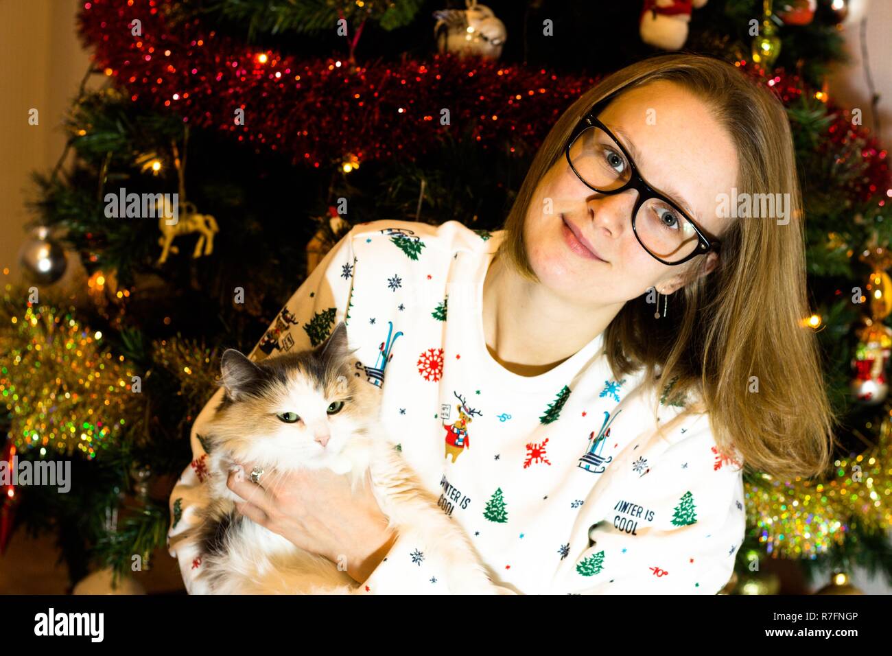 An Weihnachten und das neue Jahr Mädchen am Weihnachtsbaum sitzen mit einer Katze in den Händen. Der Baum ist in der Vorfreude auf Weihnachten dekoriert Stockfoto