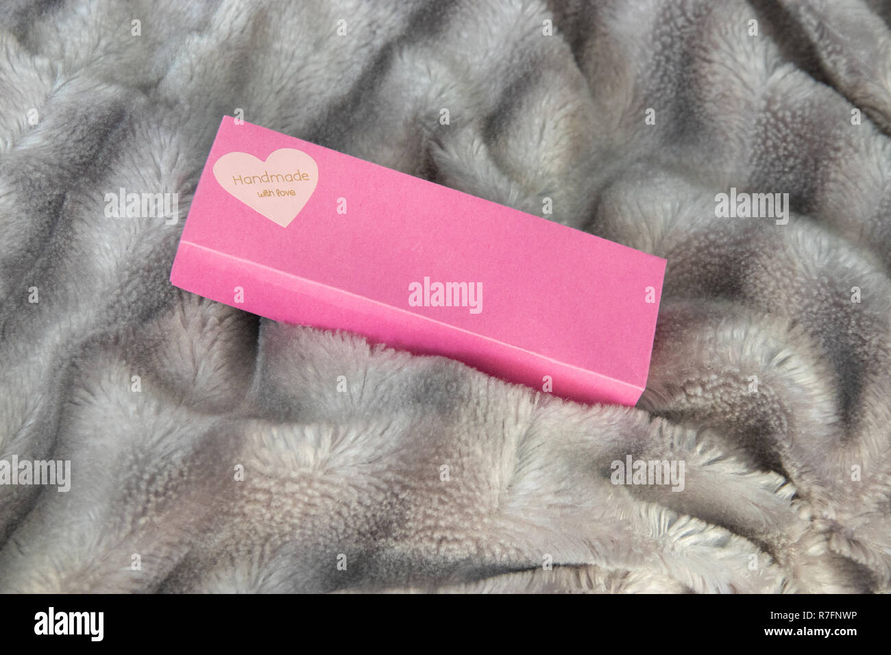 Big Pink Geschenkbox mit einem Herz voller Liebe auf das Silber Grau flauschigen Fellimitat decke Hintergrund. Label Handarbeit mit Liebe auf Herz Stockfoto