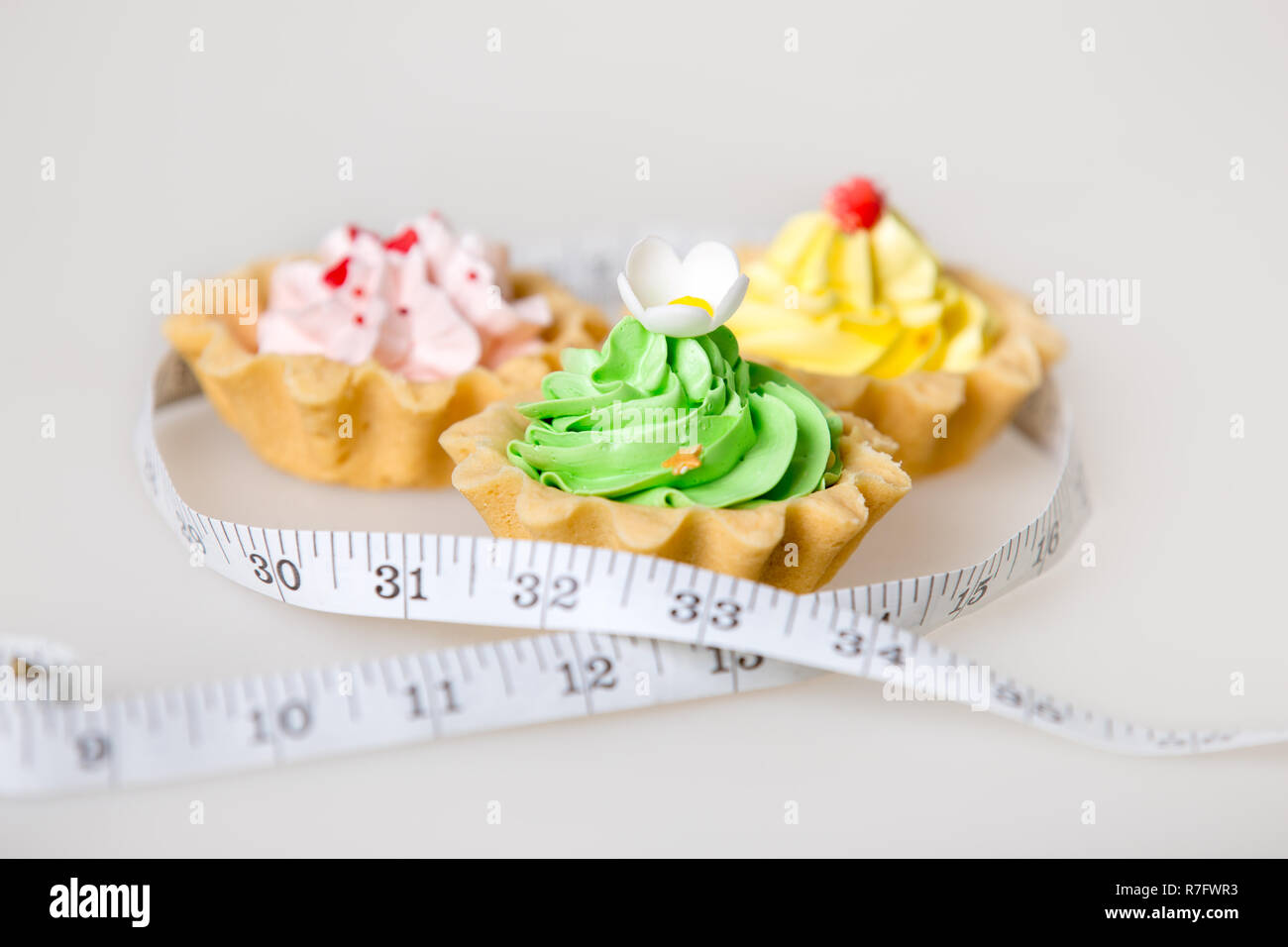 Drei farbenfrohe, grün, pink und gelb Torte Kuchen in Maßband auf weißem Hintergrund gewickelt, ungesunde Lebensweise Konzept, Studio Stockfoto