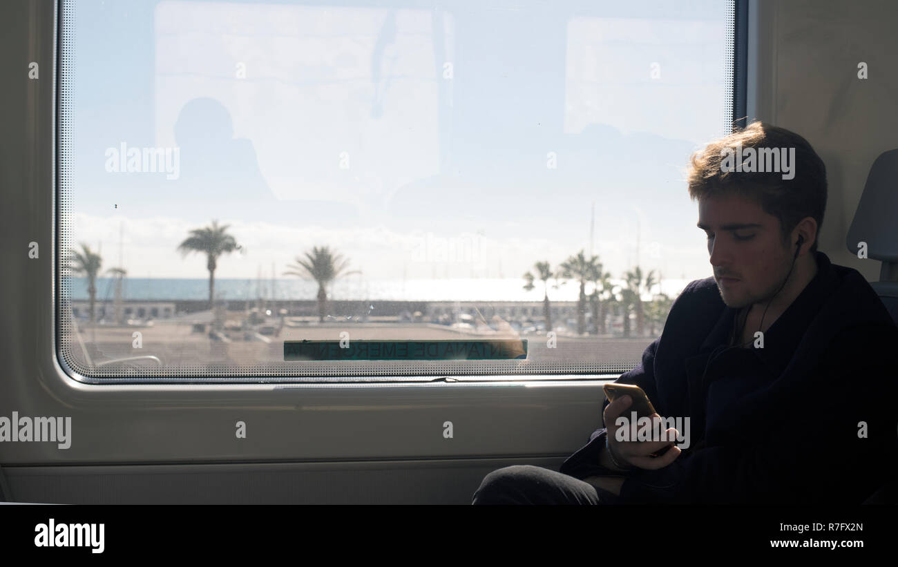 Fahrgast im Zug auf Smart Phone während der Reise entlang des Mittelmeers. Stockfoto