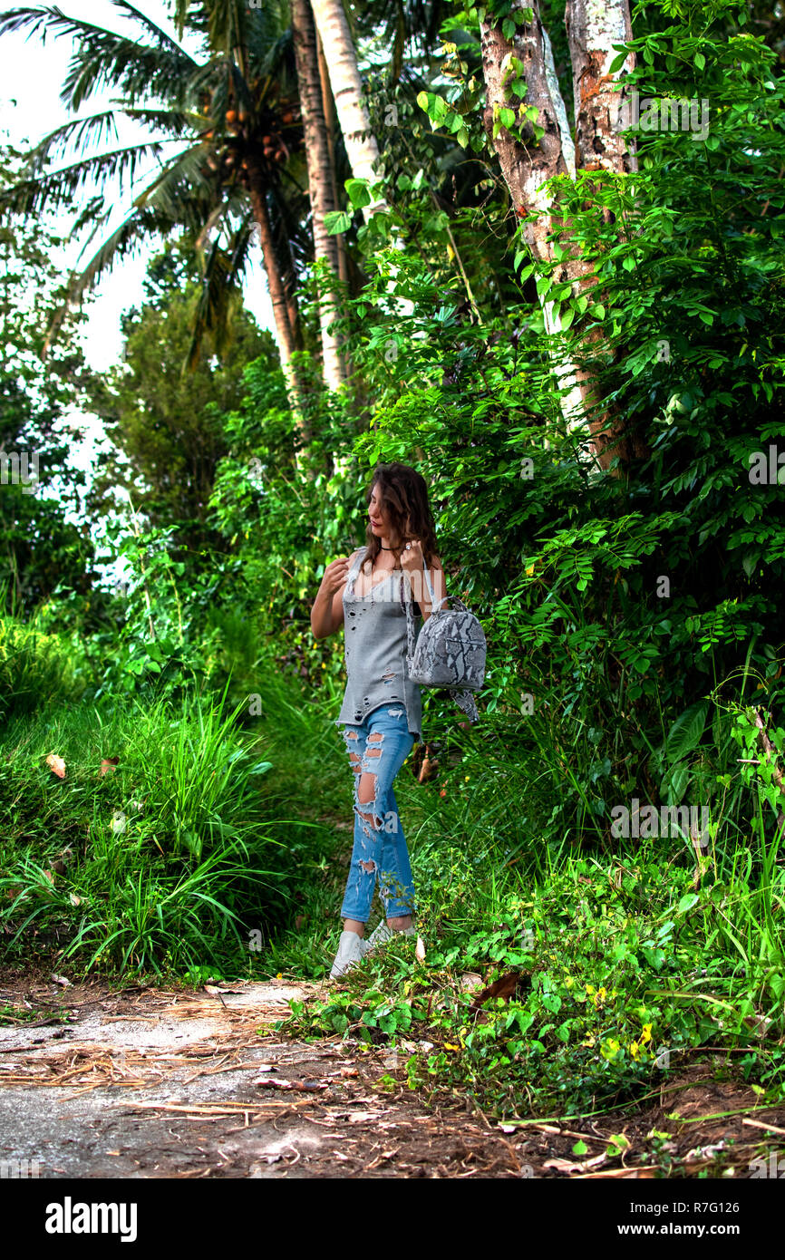 Frau gehen mit kleinen Beutel im Dschungel. Natur Hintergrund, Palmen Blätter, Holz, Jeans, Mode Stil Stockfoto