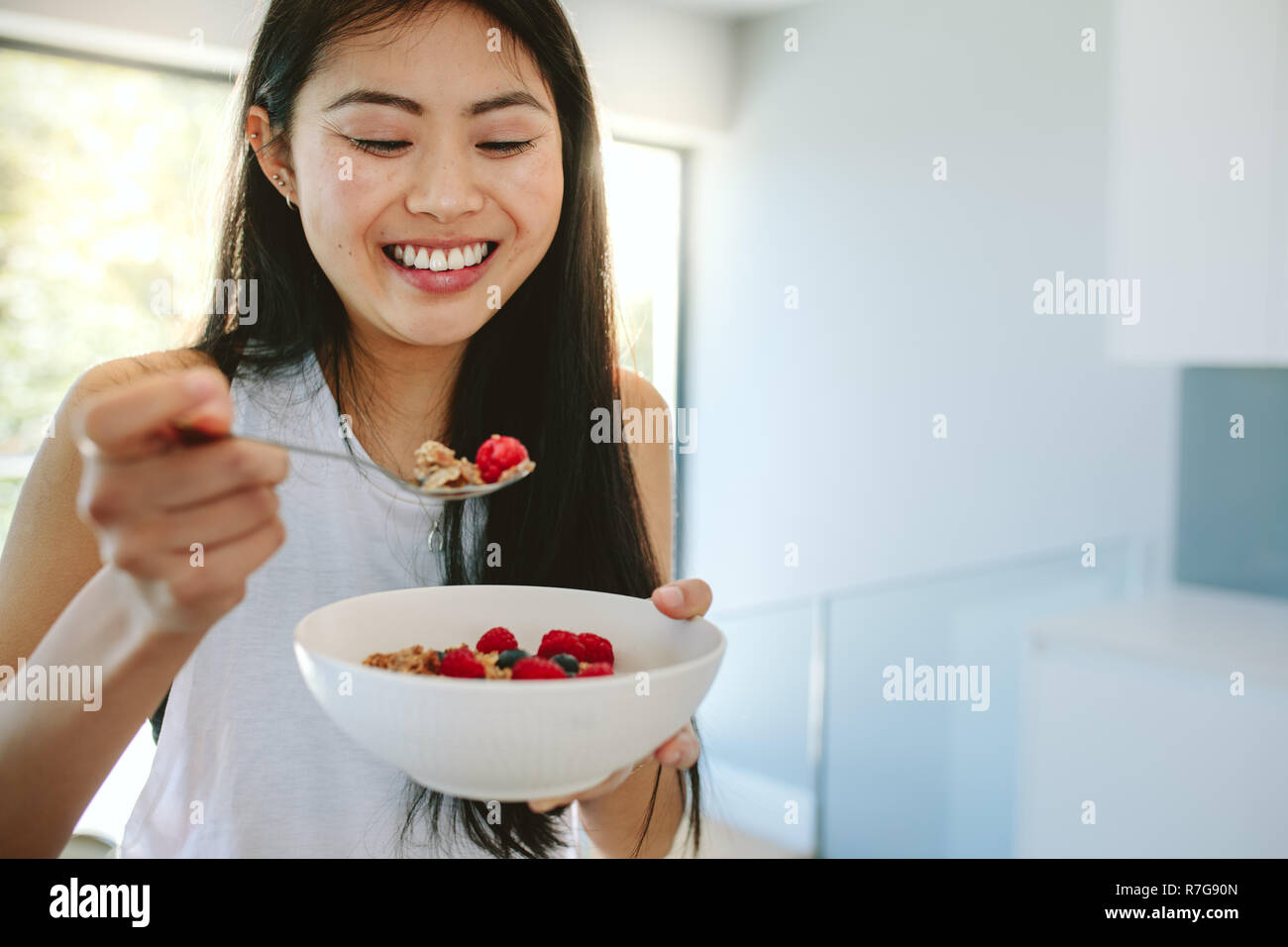 Lächelnde Frau in gesundes Frühstück zu Hause. Gesunde junge asiatische Frau in der Küche essen eine Schüssel mit nahrhaften Frühstück. Stockfoto