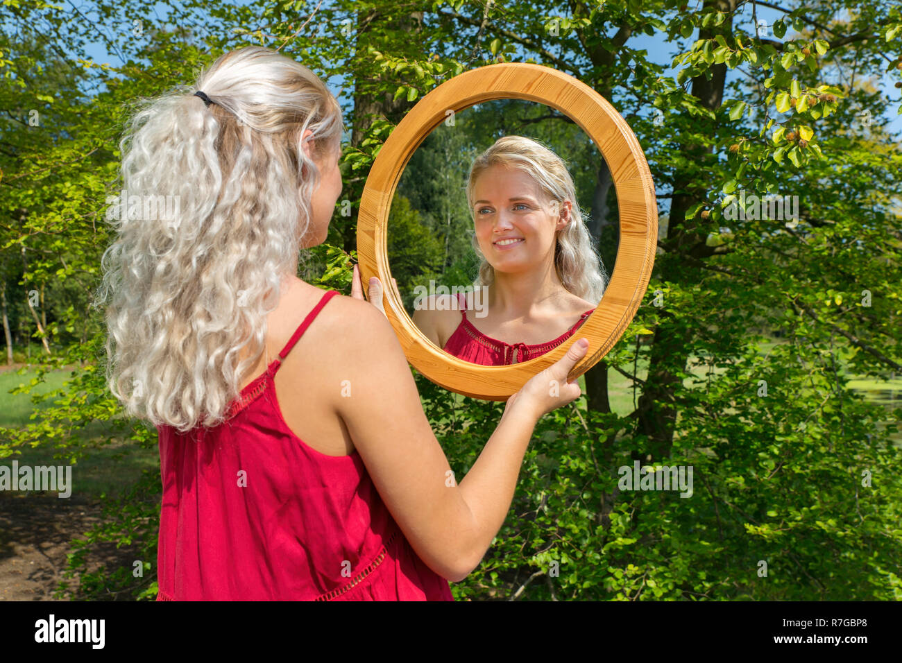 Junge blonde kaukasische Frau außerhalb in runden Holz- Spiegel Stockfoto