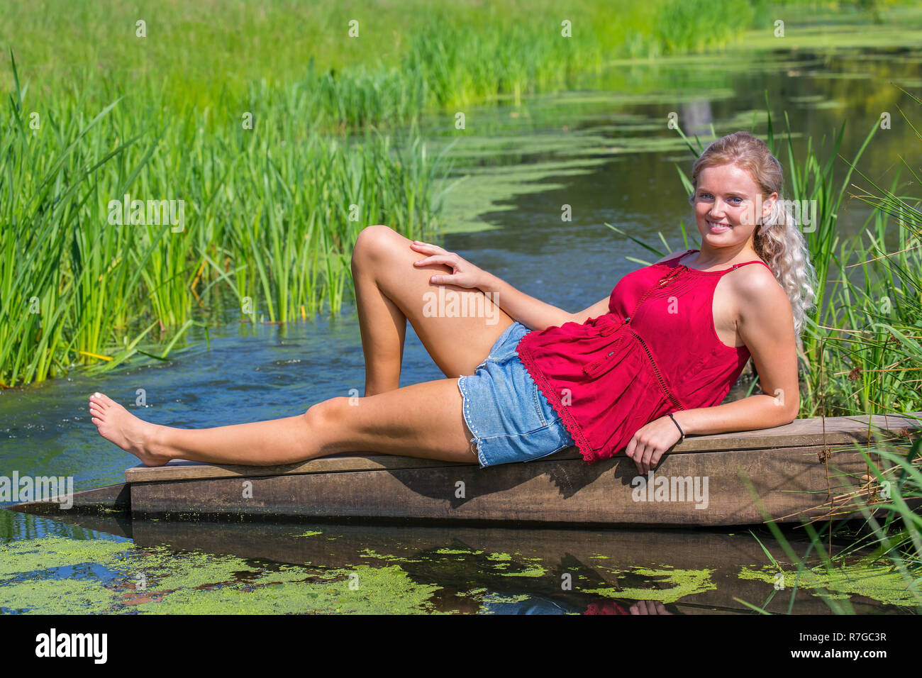 Blonde junge europäische Frau am Wasser in der Natur liegend Stockfoto