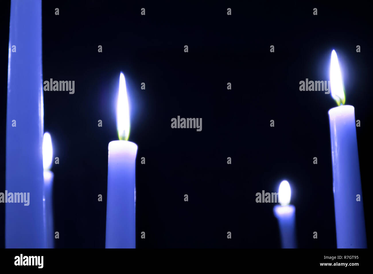 Eine Reihe von brennenden blauen Kerzen mit unscharfen Gabeln der Flamme gegen den dunklen Hintergrund Stockfoto