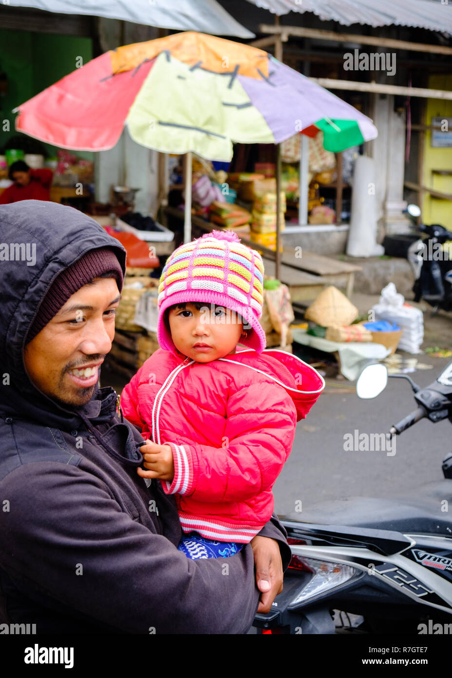 Mann und Tochter sitzen auf einem Motorrad auf einem Markt in Bali, Indonesien Stockfoto