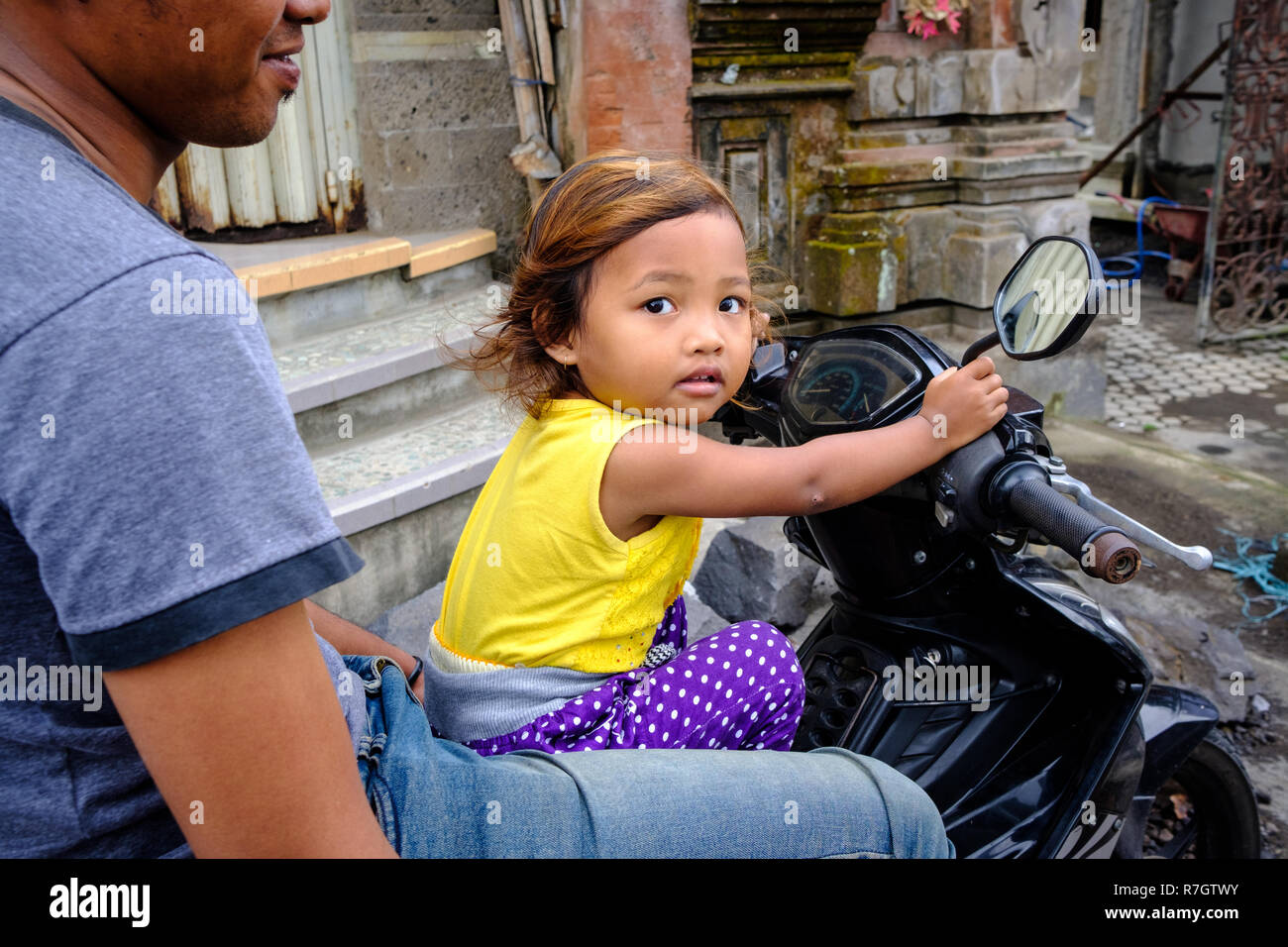 Mann und Tochter sitzen auf einem Motorrad auf einem Markt in Bali, Indonesien Stockfoto