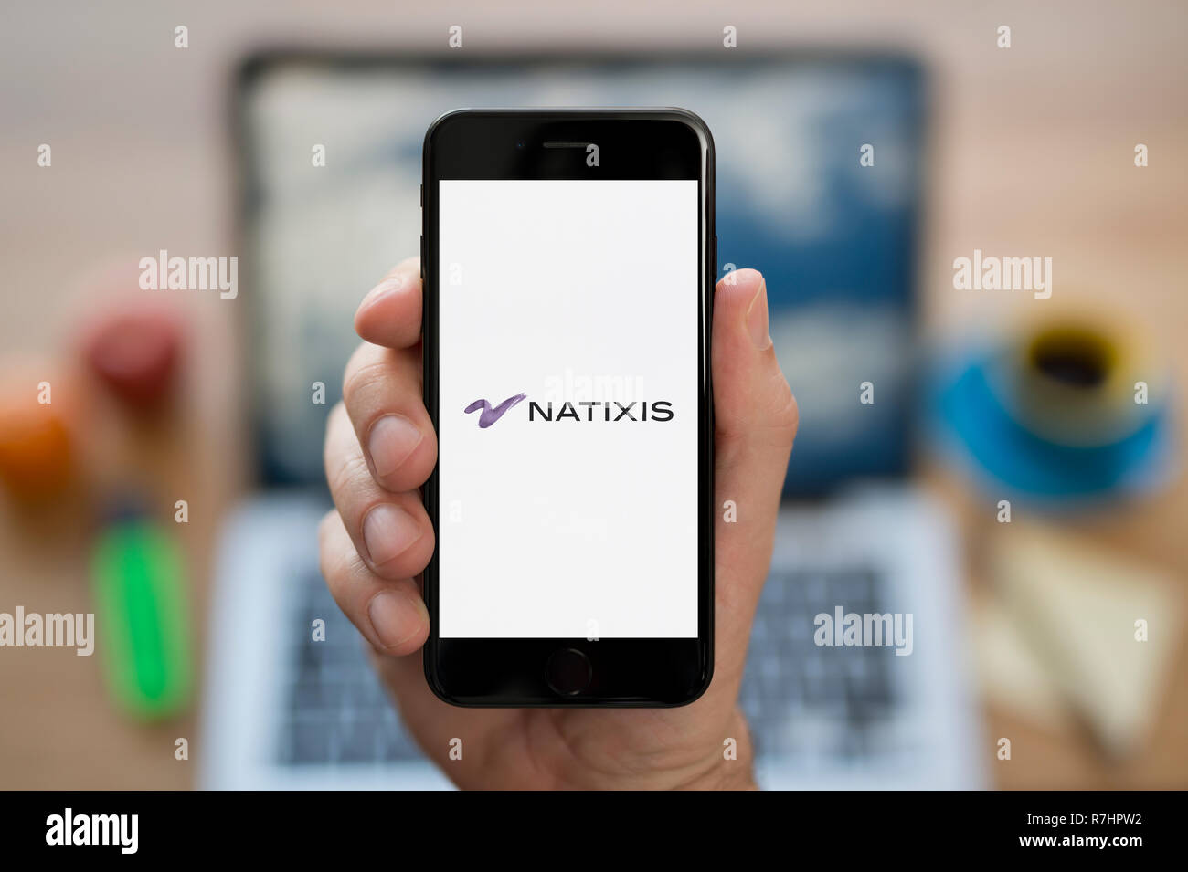 Ein Mann schaut auf seinem iPhone die zeigt die Natixis Logo (nur redaktionelle Nutzung). Stockfoto