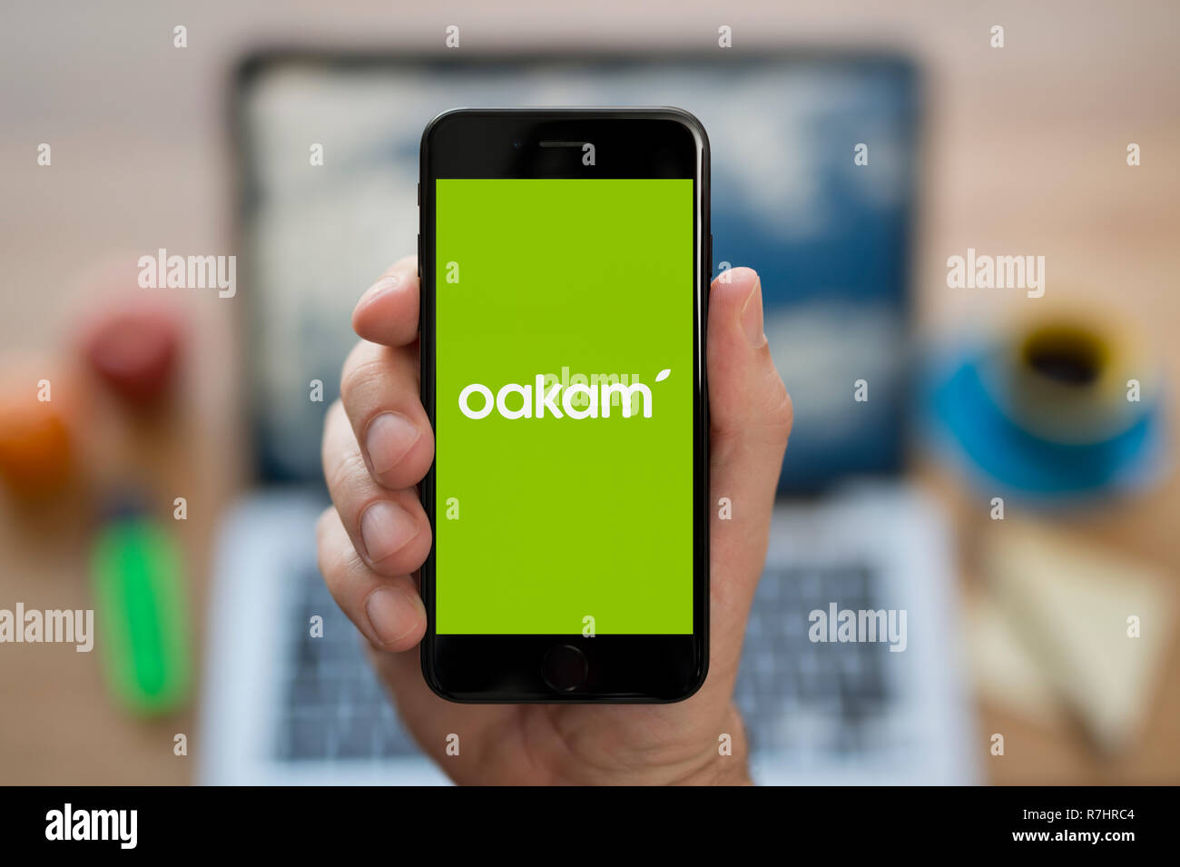 Ein Mann schaut auf seinem iPhone die zeigt die Oakam Logo (nur redaktionelle Nutzung). Stockfoto