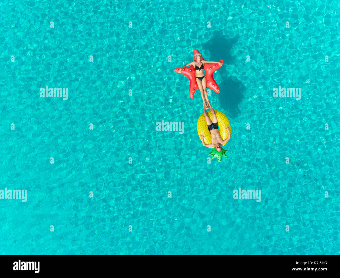 Luftaufnahme von Mann und Frau auf aufblasbaren Matratzen berühren die Füße auf transparenten Meer. Stockfoto