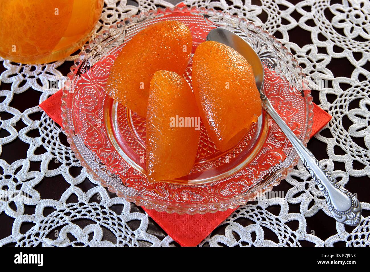 Closeup hausgemachte Bitter Orange Dessert in einem durchsichtigen kleinen Teller mit einem Löffel über ein rotes Papier Handtuch auf eine weiße Stickerei Tischdecke in der Nähe eines Jar Stockfoto