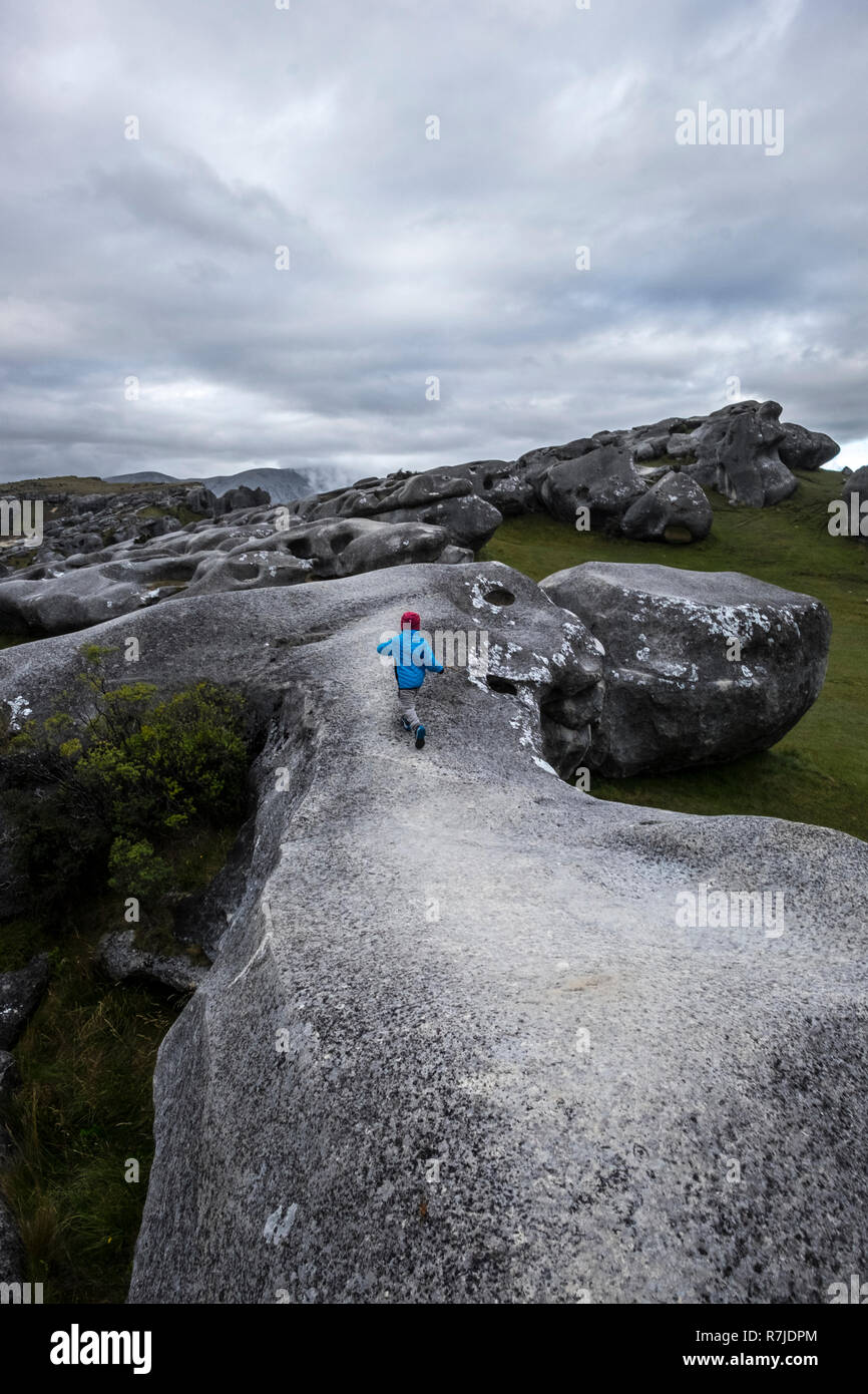 Neuseeland Castle Hill. Kleines Mädchen laufen weg auf den Felsen. Bewölkter Himmel. Grauen rock. Blaue Kleidung. Hut lesen. National Park. Arthurus Berge. Kind. Stockfoto