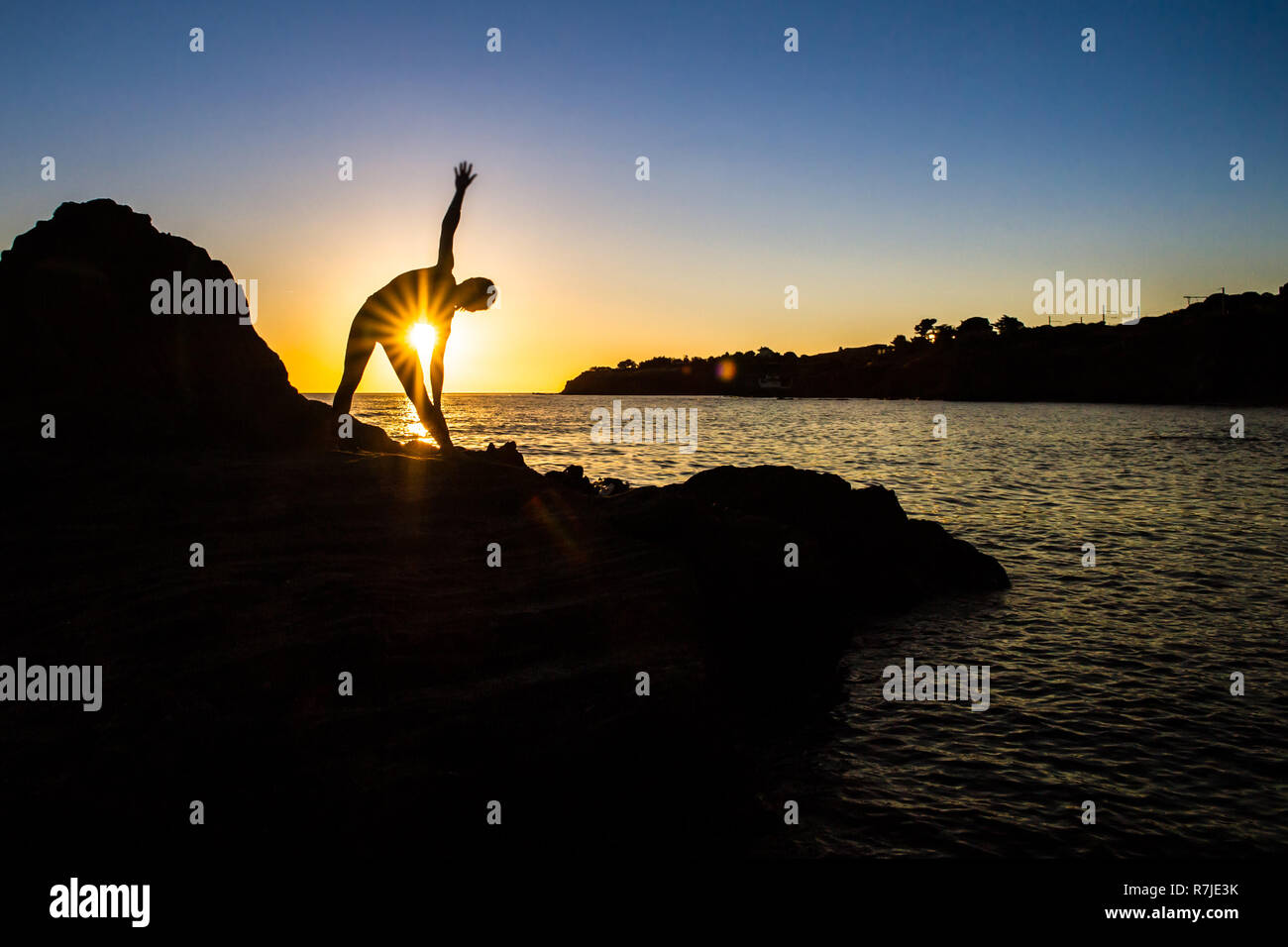 Argelès-sur-Mer (Frankreich). Jemand Yoga auf den Felsen vor der Racou Strand bei Sonnenaufgang. Schöne junge Frau mit langen b Stockfoto