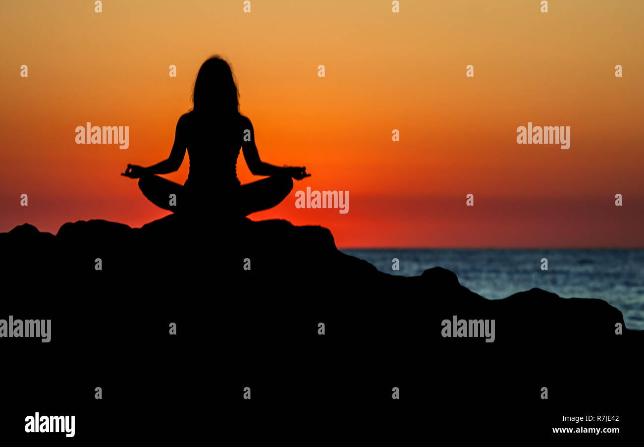 Argelès-sur-Mer (Frankreich). Jemand Yoga auf den Felsen vor der Racou Strand bei Sonnenaufgang. Schöne junge Frau mit langen b Stockfoto