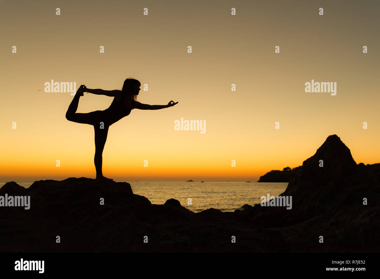 Argelès-sur-Mer (Frankreich). Jemand Yoga auf den Felsen vor der Racou Strand bei Sonnenaufgang. Schöne junge Frau mit langen b Stockfoto