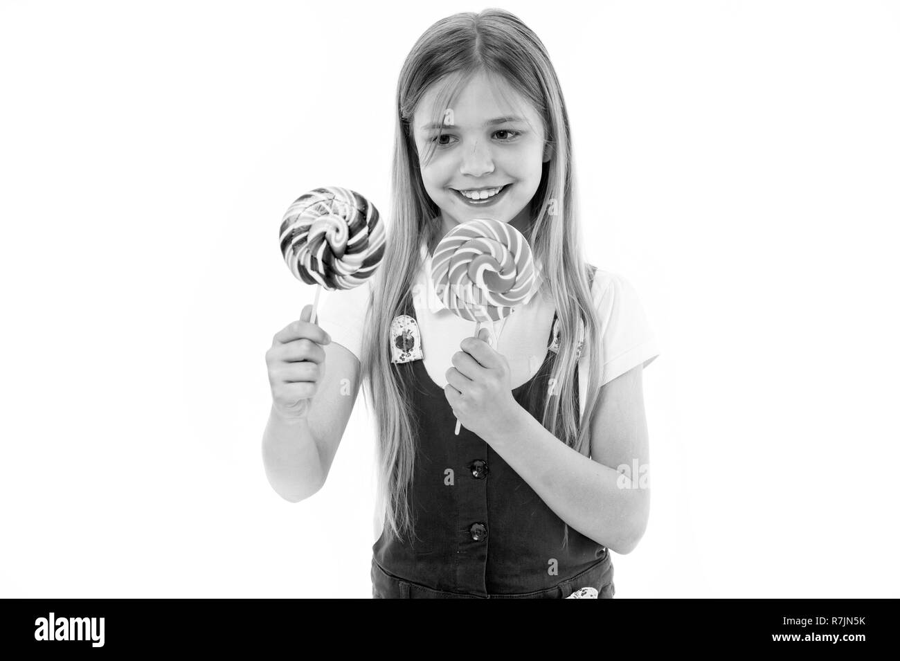 Harte Wahl. Fröhliches kleines Mädchen holding Lutscher in der Hand und lächelt beim Stehen isoliert auf Weiss. Mädchen können sich nicht entscheiden, welche Lollipop sie will. Süßigkeiten süchtig Kid will alle Süßigkeiten. Stockfoto