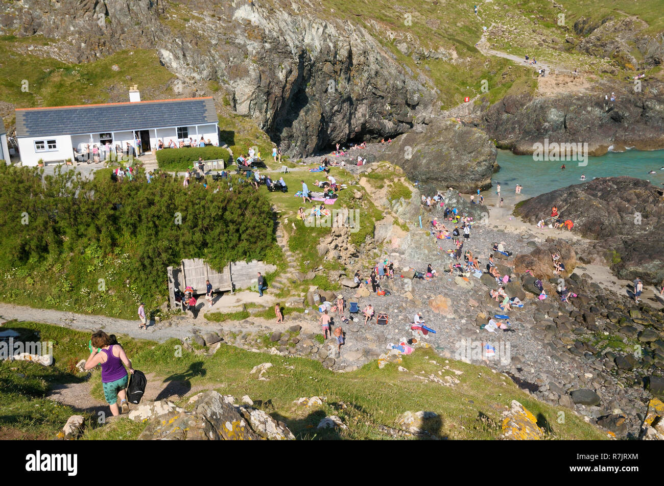 Touristen zum Sonnenbaden an den felsigen Küsten von Kynance Cove neben dem Cafe, Cornwall, England, Großbritannien Stockfoto