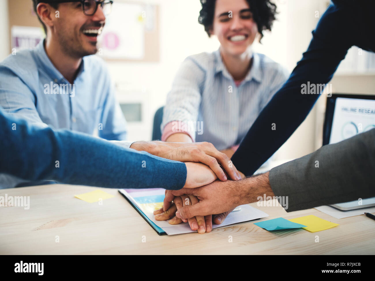 Junge Geschäftsleute sitzen um den Tisch in einem modernen Büro, Stapeln die Hände. Stockfoto