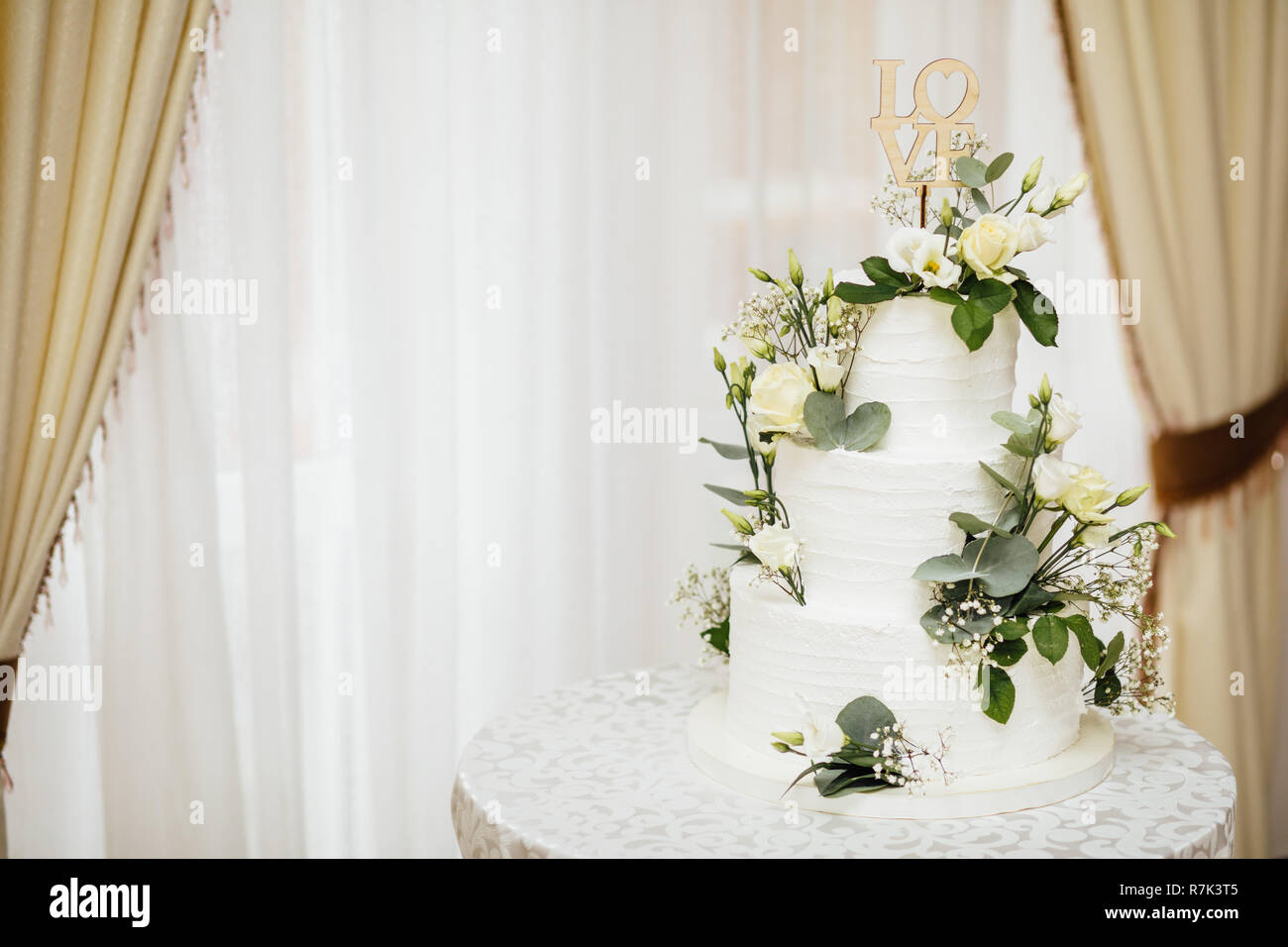 Weisse Hochzeitstorte mit Blumen. Das Wort Liebe mit Herz. Stockfoto