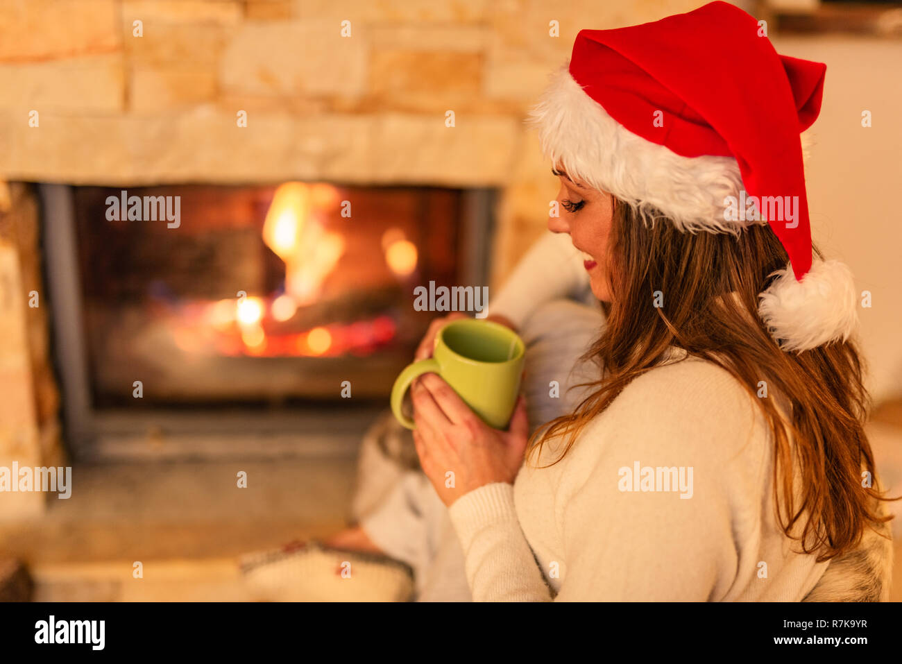 Schöne junge lächelnde Frau genießen eine Tasse Tee vor dem Kamin in Weihnachten Abend. Stockfoto